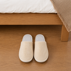 Luxury coral fleece hotel slippers beside hotel bed