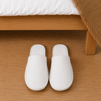 Waffle cotton hotel guest slippers beside hotel bed