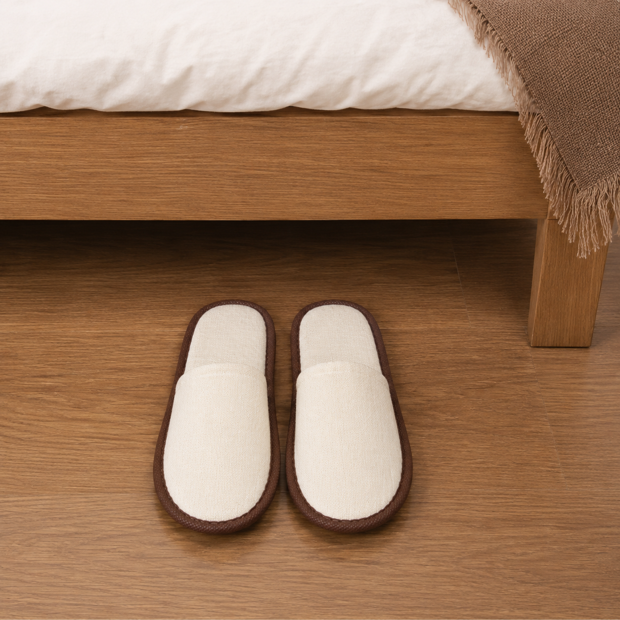 Premium linen hotel slippers placed beside hotel bed